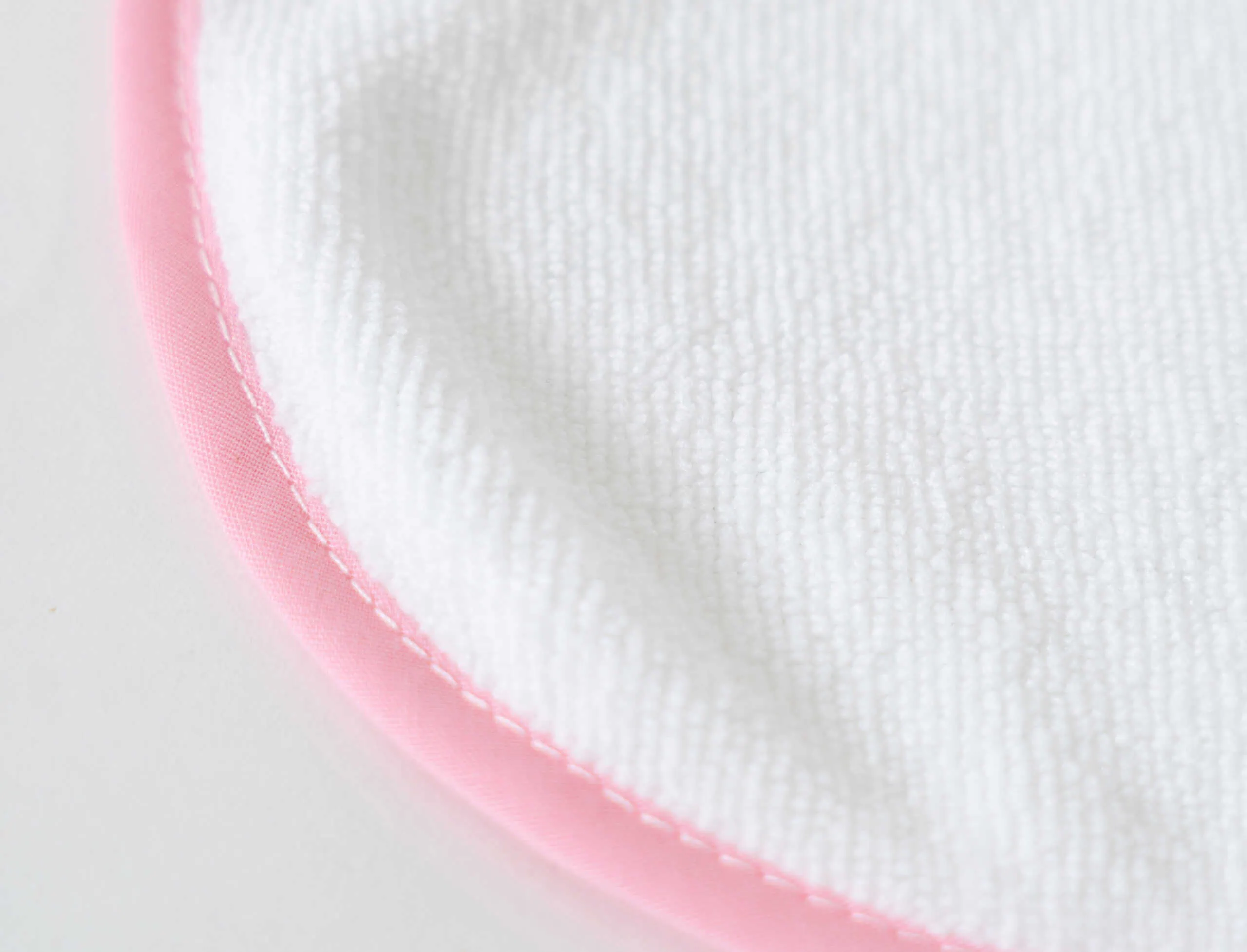 babete_rosa Alto texto: Detalhe de tecido branco com acabamento rosa, enfatizando artigos de higiene para bebés.
